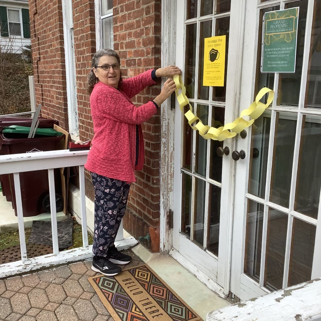 Photo of Berta Winiker cutting a paper chain ribbon at library back door.